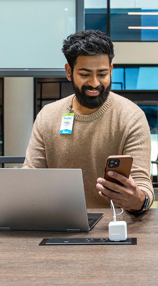 A happy Clayton employee works in a newly renovated workspace on their phone and laptop.